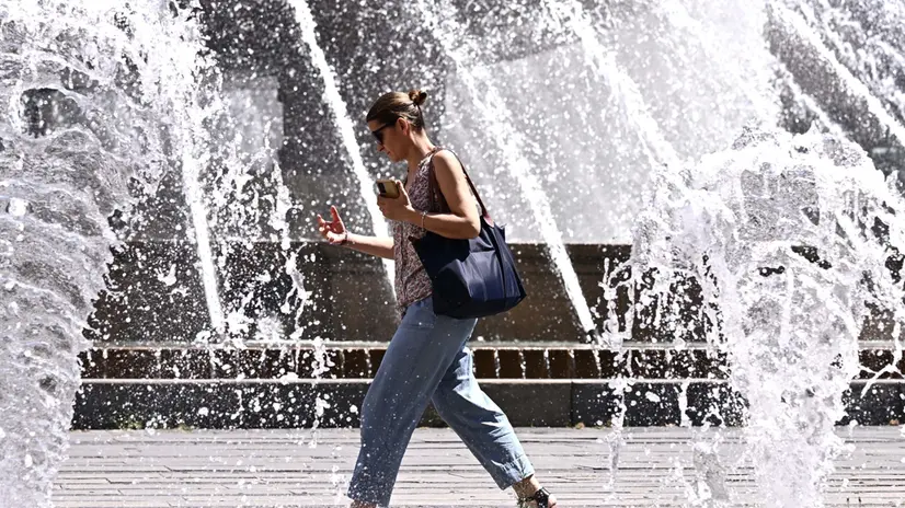 Una turista sotto il sole cocente in pieno centro citta', dalla fontana di piazza De Ferrari. Genova, 01 luglio 2025. ANSA/LUCA ZENNARO