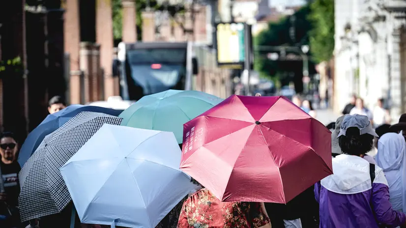 Turisti giapponesi con l'ombrello in piazza San Giovanni in cerca di refrigerio per combattere le alte temperature dovute all'ondata di caldo estivo. Torino 28 giugno 2025 ANSA/TINO ROMANO