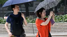 Turisti camminano utilizzando ombrelli per proteggresi dal sole mentre fotografano con i loro smartphone la fontana diPiazza Castello, Milano, 13 giugno 2025. ANSA/DANIEL DAL ZENNARO