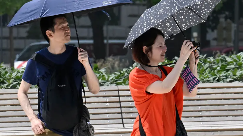 Turisti camminano utilizzando ombrelli per proteggresi dal sole mentre fotografano con i loro smartphone la fontana diPiazza Castello, Milano, 13 giugno 2025. ANSA/DANIEL DAL ZENNARO