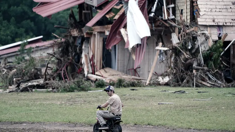 epa12221132 A person rides a mini bike past a house damaged from flood waters in Hunt, Texas, USA, 06 July 2025. At least 59 people have been killed after floodwaters swept through a summer camp and nearby homes on early 04 July. EPA/DUSTIN SAFRANEK