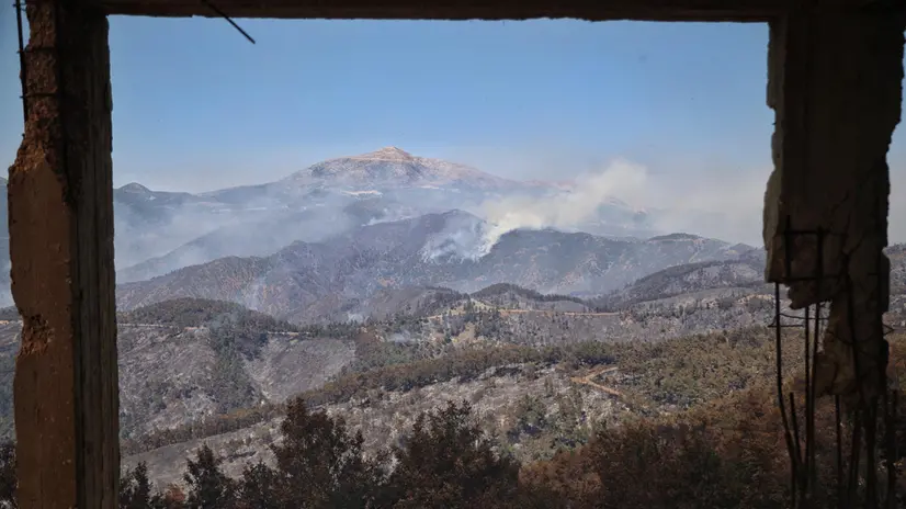 epa12233129 Mountains burn from the wildfires is seen through the interior of a damaged building hit during previous years of conflict in Latakia, Syria, 11 July 2025. Since 30 June, wildfires in Latakia have burned over 15,000 hectares, prompting the UN to allocate 625,000 US dollars from the Syria Humanitarian Fund for emergency response. EPA/Bilal Al-hammoud