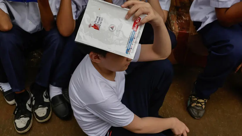 epa12184593 A student covers his head with a notebook indicating an emergency hotline number during an earthquake drill at an elementary school in Quezon City, Metro Manila, Philippines, 19 June 2025. The Philippines conducted the second quarterly nationwide earthquake drill on 19 June, as authorities remind the public to actively participate in emergency exercises to improve responses in times of actual disasters. EPA/ROLEX DELA PENA