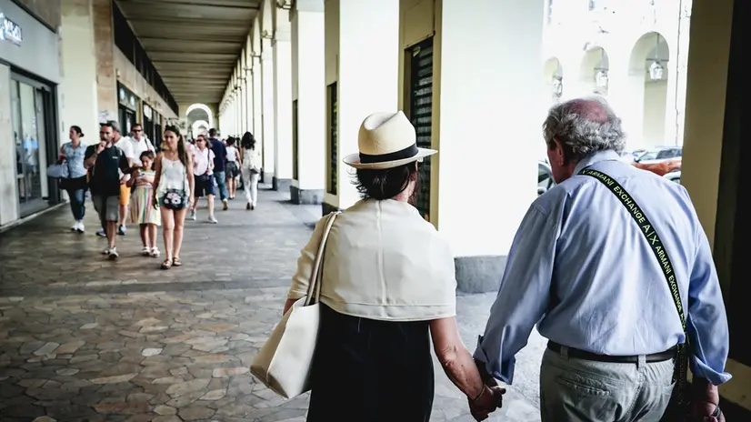 Due anziani si tengono per mano passeggiando sotto i portici di via Po in una giornata afosa estiva. Torino 22 giugno 2025 ANSA/TINO ROMANO