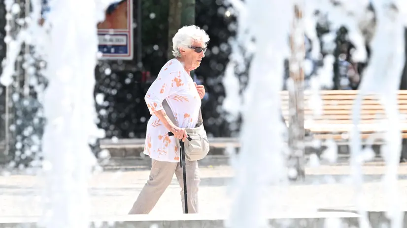 Un'anziana passeggia accanto a una fontana nel centro di Milano, 24 luglio 2024. Alta pressione sul nostro Paese almeno fino al 10 agosto con temperature elevate ed il ritorno del caldo africano. ANSA/DANIEL DAL ZENNARO