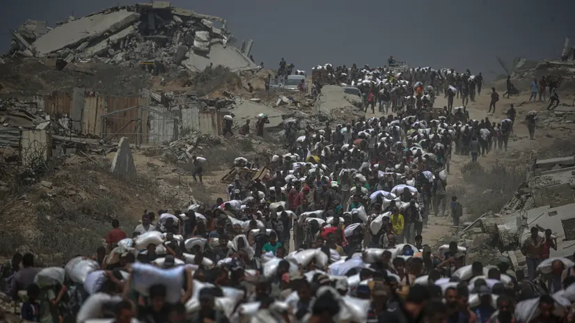 epa12266154 Internally displaced Palestinians carry bags of flour near a food distribution point in Zikim, northern Gaza Strip, 27 July 2025. The Israeli army declared a 'tactical pause' in military operations in parts of the Gaza Strip on 27 July, to facilitate the safe passage of humanitarian aid convoys. More than 130 Palestinians, the majority of whom children, have died of malnutrition in the Gaza Strip, the Palestinian Ministry of Health said on 27 July. EPA/MOHAMMED SABER