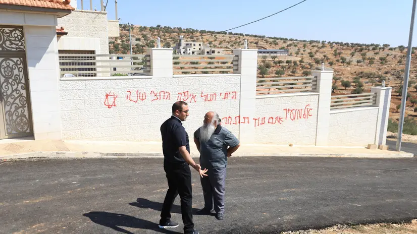 epa12268114 Paletinians talk in front of a spray-painted graffito reading "Al-Mughayyir, you will regret it later" in the Palestinian Christian viilage of Taybeh near the West Bank city of Ramallah, 28 July 2025. According to the Palestinian news agency Wafa, Israeli settlers attacked the village of Taybeh and set two vehicles on fire and spray-painted racist slurs on walls. EPA/ALAA BADARNEH