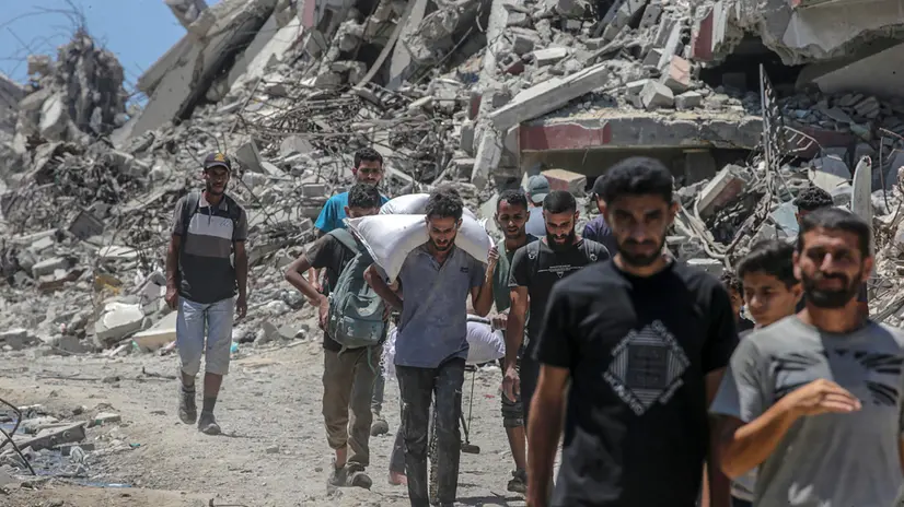 epa12249940 Palestinians carry bags of flour along Rashid Road in western Jabalia, northern Gaza Strip, 20 July 2025. According to the Palestinian Ministry of Health in Gaza, at least 67 people were killed while trying to receive humanitarian aid in the Zikim area, northern Gaza. EPA/MOHAMMED SABER