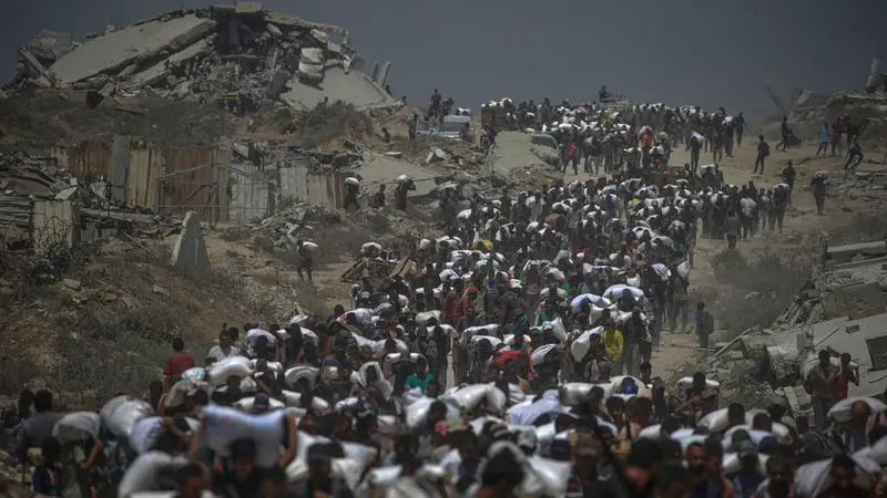 epa12266154 Internally displaced Palestinians carry bags of flour near a food distribution point in Zikim, northern Gaza Strip, 27 July 2025. The Israeli army declared a 'tactical pause' in military operations in parts of the Gaza Strip on 27 July, to facilitate the safe passage of humanitarian aid convoys. More than 130 Palestinians, the majority of whom children, have died of malnutrition in the Gaza Strip, the Palestinian Ministry of Health said on 27 July. EPA/MOHAMMED SABER