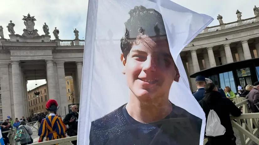 Un gruppo di ragazzi provenienti dalla Germania sventola bandiere con il volto di Carlo Acutis sul lato sinistro di piazza San Pietro in occasione dei funerali di Papa Francesco, Città del Vaticano, 26 aprile 2025. ANSA/MARIA ELENA MARSICO (funerali, esequie, messa)
