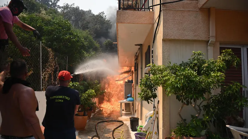 epa12297498 Firefighters and residents battle to put out a fire burning a house during a wildfire in Vounteni village, Achaia, Peloponnese, Greece, 13 August 2025. The wildfires in the Syhena area of Patras and in Western Achaia continued to burn unchecked on Wednesday. In Western Achaia, the fire was also ongoing, with strong firefighting forces battling the flames. In total, 165 firefighters, five ground teams, and 51 fire engines were operating in the area. EPA/GIOTA LOTSARI