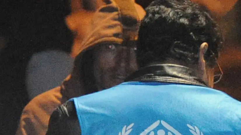 Un operatore dell'Unhcr assiste i migranti appena sbarcati a Lampedusa, Agrigento, 12 febbraio 2011. Infreddoliti, stanchi per il lungo viaggio, ma contenti di essere arrivati in Italia: i 107 immigrati giunti poco fa nel porto di Lampedusa hanno applaudito appena la loro imbarcazione ha ormeggiato ed hanno salutato i giornalisti presenti sul molo facendo il segno di 'vittoria' con le dita. ANSA / CIRO FUSCO