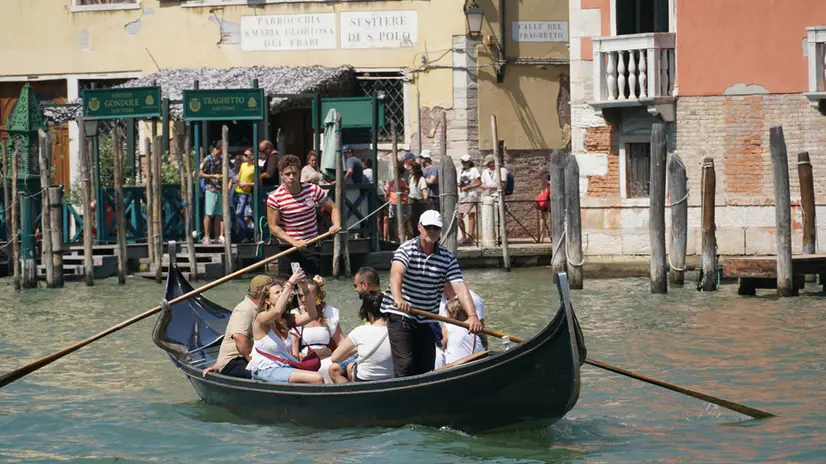 Alcuni turisti sulla gondola da “parada” del traghetto pubblico di San Tomà, nel sestiere di San Polo, per attraversare il Canal Grande in pochi minuti , raggiungendo rapidamente l’area marciana, sulla riva opposta, Venezia 12 agosto 2025. ANSA/ANDREA MEROLA