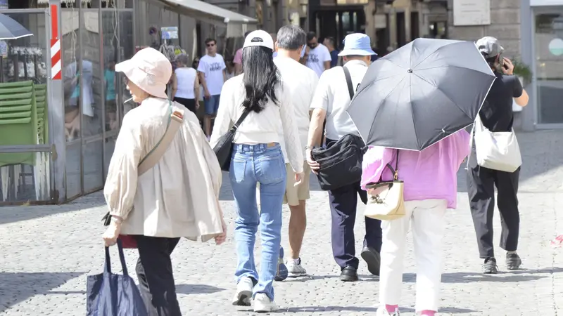 Turisti in piazza Chanoux ad Aosta si riparano dal caldo con copricapo e ombrelli. Aosta, 13 agosto 2025. Generica simbolica afa estate turismo turista ombrello centro storico