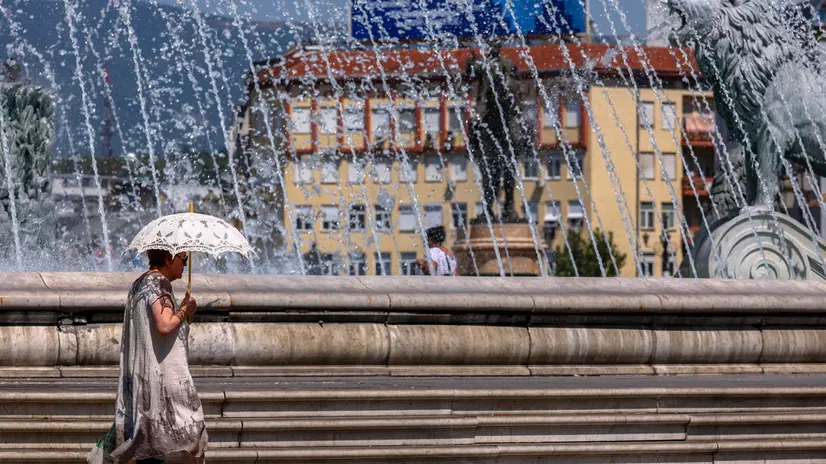 epa12293657 A woman shelters from the sun under an umbrella as she walks past a fountain during a heatwave in Skopje, North Macedonia, 11 August 2025. The country is under the influence of a very warm air mass from northern Africa, with temperatures expected to climb up to 40 degrees Celsius. EPA/GEORGI LICOVSKI
