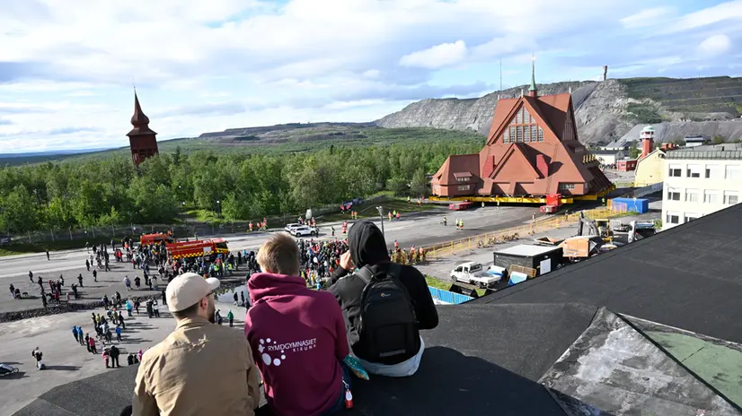 epa12309349 People watch as the Kiruna Church landmark is being moved on a specially designed trolley with 224 wheels at a speed of half a kilometer per hour in Kiruna, northern Sweden, 19 August 2025. The 40-meter-wide, 672,000-kilo wooden church has been placed on a wheeled trailer for its five-kilometre relocation to Kiruna's new town center on 19 and 20 August, due to the expansion of the iron ore mine. EPA/Fredrik Sandberg SWEDEN OUT