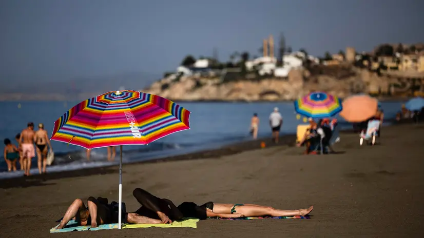 epa12297286 People relax under a parasol at El Rincon de la Victoria beach in Malaga, Spain, 13 August 2025. The Spanish Meteorology Agency (AEMET) has issued an orange alert in five regions across the country due to the high temperatures expected in the heat wave affecting the Peninsula. EPA/JORGE ZAPATA