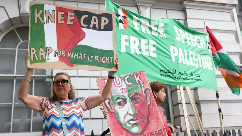 epa12311869 A supporter of Kneecap's Liam O'Hanna holds a placard in front of flags outside Westminster Magistrates' Court ahead of his appearance in court in London, Britain, 20 August 2025. The musician, known as Mo Chara and also as Liam Og O hAnnaidh, appeared in court on a terrorism charge for displaying a Hezbollah flag at a November 2024 gig. EPA/NEIL HALL