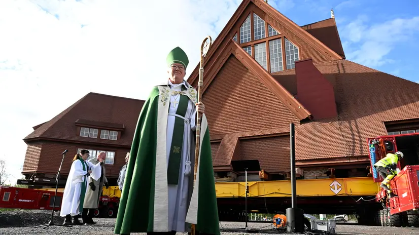 epa12309249 Asa Nystrom, Bishop of Lulea Diocese, blesses the Kiruna Church landmark that is being moved on a specially designed trolley with 224 wheels at a speed of half a kilometer per hour in Kiruna, northern Sweden, 19 August 2025. The 40-meter-wide, 672,000-kilo wooden church has been placed on a wheeled trailer for its five-kilometre relocation to Kiruna's new town center on 19 and 20 August, due to the expansion of the iron ore mine EPA/Fredrik Sandberg SWEDEN OUT
