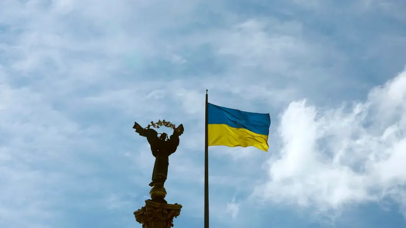 epa12317944 A Ukrainian flag flutters next to the Independence Monument at the Independence Square in downtown Kyiv, Ukraine, 23 August 2025. Ukraine marked the National Flag Day amid the ongoing Russian invasion. Ukraine celebrates the National Flag Day on 23 August every year. EPA/SERGEY DOLZHENKO