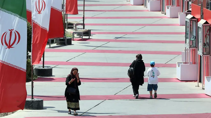 epa12329187 Iranians walk next to Iran’s national flags in a street in Tehran, Iran, 28 August 2025. EPA/ABEDIN TAHERKENAREH