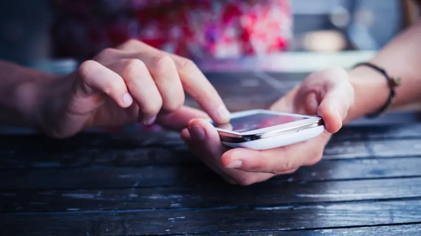 A young woman is using her smart phone at a table outside