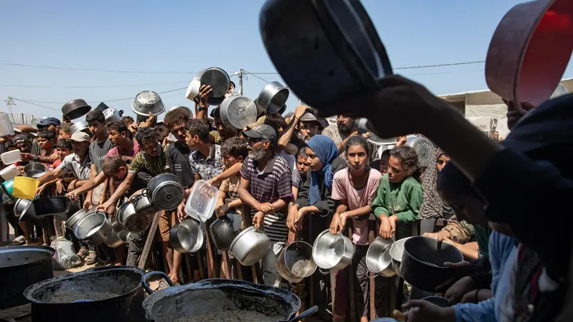 epaselect epa12317922 Palestinians queue to receive a meal from a kitchen that provides free food for displaced people in Khan Yunis, southern Gaza Strip, on 23 August, 2025. EPA/HAITHAM IMAD