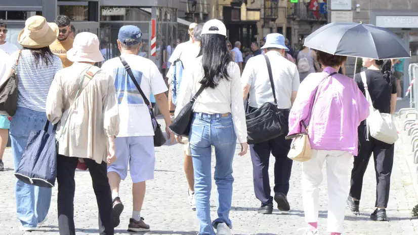 Turisti in piazza Chanoux ad Aosta si riparano dal caldo con copricapo e ombrelli. Aosta, 13 agosto 2025. Generica simbolica afa estate turismo turista ombrello centro storico