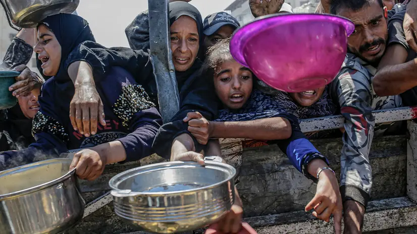 epa12282740 Internally displaced Palestinians, including children, hold pots as they gather to receive food from a charity kitchen, in Gaza City, Gaza Strip, 04 August 2025. Humanitarian organizations have warned of an imminent food catastrophe for thousands of children, a crisis caused by severe food insecurity, a decline in health services, and ongoing restrictions on humanitarian aid and essential supplies. EPA/MOHAMMED SABER