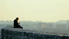 Una ragazza da sola mentre guarda lo smartphone - © www.giornaledibrescia.it