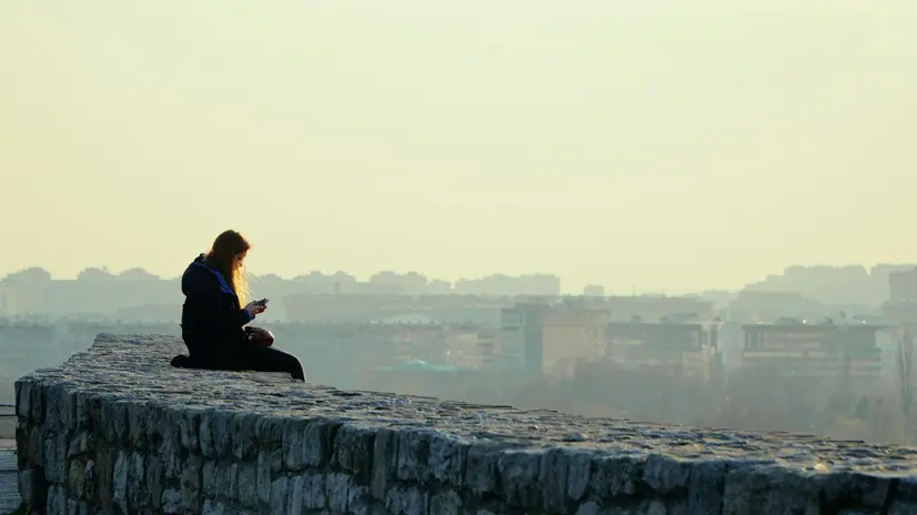 Una ragazza da sola mentre guarda lo smartphone - © www.giornaledibrescia.it
