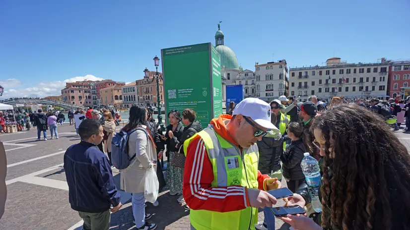 Un’operatore ai varchi controlla il ticket di accesso sul telefonino di un turista, al check point del piazzale della stazione ferroviaria, Venezia 25 aprile 2024. ANSA/ANDREA MEROLA