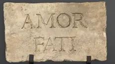 Una lapide su cui è scolpita l'espressione «Amor fati» - © www.giornaledibrescia.it