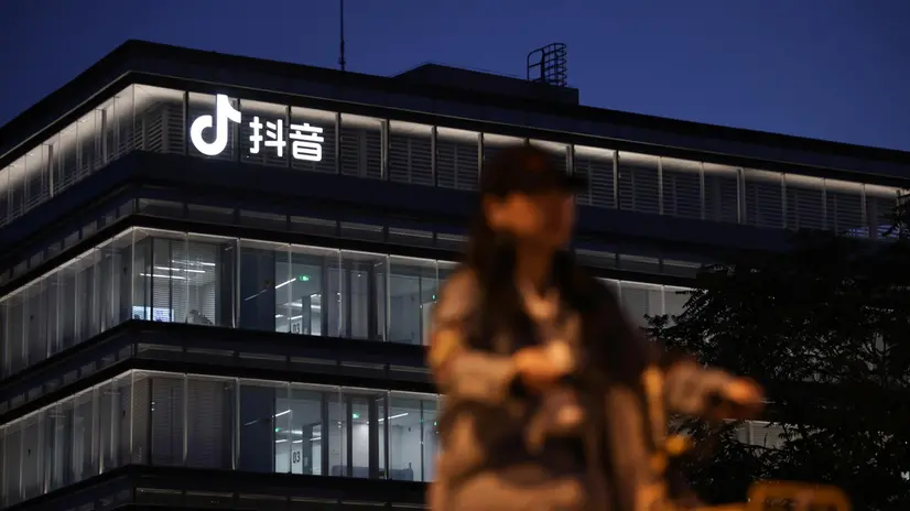 epa12389662 A woman rides a bicycle past a building with the Douyin logo in Beijing, China, 19 September 2025. The Douyin app is the Chinese counterpart of TikTok. The US and the Chinese presidents on 19 September were expected to hold a phone call to finalize a deal allowing social media app TikTok to continue operating in the US, among other topics. EPA/ANDRES MARTINEZ CASARES