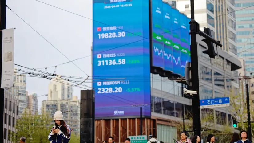 epa12015255 People walk on a street near screens showing stock exchange and economic data in Shanghai, China, 07 April 2025. Hong Kong and Chinese stocks plummeted dramatically on April 7 after Beijing countered US tariffs with its own set of trade levies. The move sent shock waves through financial markets, igniting fears among investors of an expanding trade war that could plunge the global economy into a severe recession. EPA/ALEX PLAVEVSKI