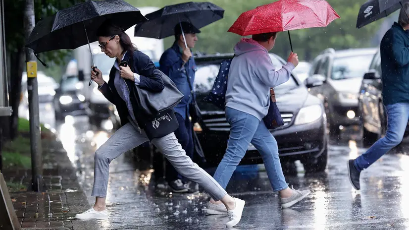 epa12384553 A woman holding an umbrella jumps over a puddle formed after heavy rain while crossing the street in Bucharest, Romania, 17 September 2025. EPA/ROBERT GHEMENT