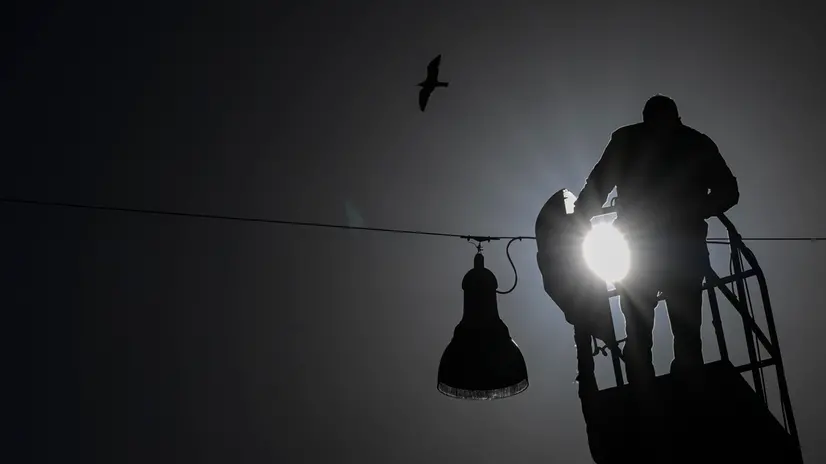 Un uomo impegnato nella manutenzione di un lampione stradale a Napoli, 25 novembre 2024. ANSA/CIRO FUSCO (simbolica, generica, uomo, controluce, silhouette, lavoratore, gru, scala)