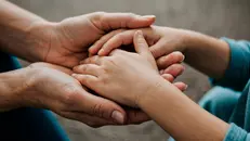 Mani di un bambino tra quelle d un adulto (immagine simbolica) - © www.giornaledibrescia.it