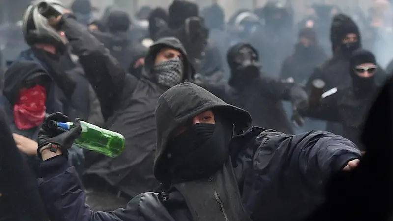 Un black bloc ripreso in primo piano mentre lancia una bottiglia a Milano nel 2015 - Foto Ansa © www.giornaledibrescia.it